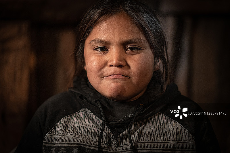 在霍根小屋里试图保持温暖，表情严肃的年轻美洲原住民男孩的艺术肖像图片素材
