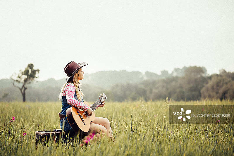坐在草地上弹吉他的金发女牛仔图片素材