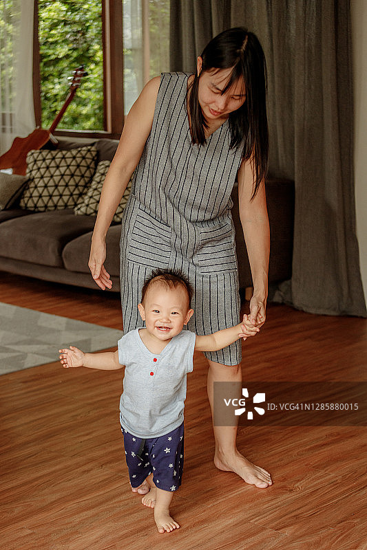 快乐的小宝宝在客厅里学习走路，妈妈在一旁帮助图片素材