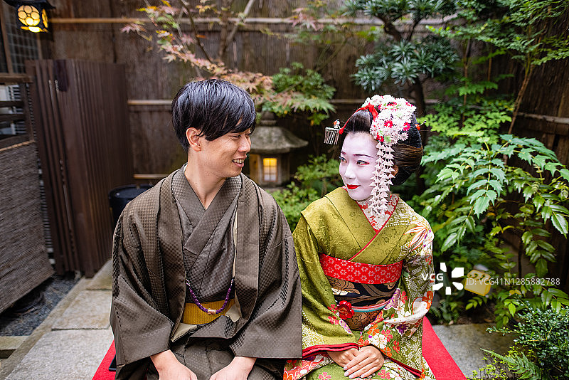 日本庭院中，舞妓和穿着袴的年轻男子对坐图片素材