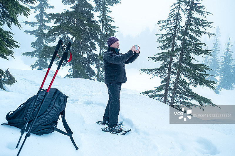 中年男人穿着雪鞋用智能手机拍照图片素材