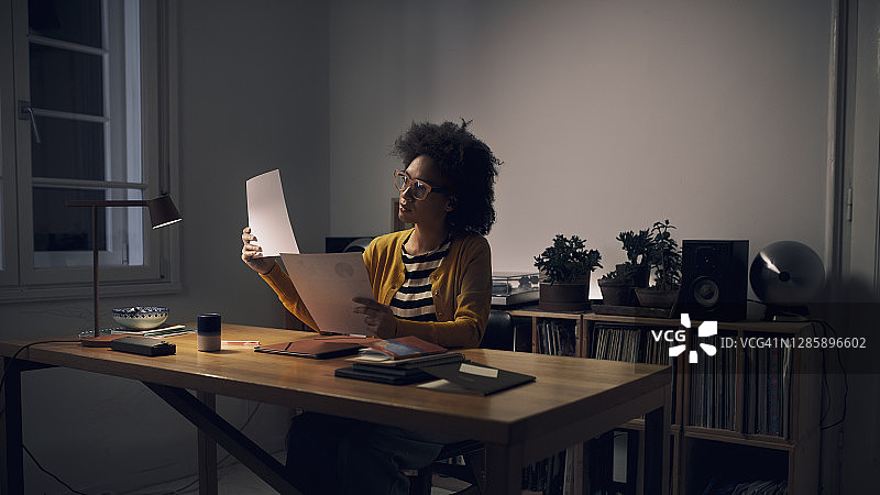 深夜在家工作：一位年轻的非裔美国妇女坐在家庭办公室里阅读文件图片素材