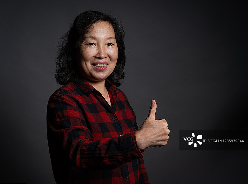 在深色背景下竖起大拇指的年长女性图片素材