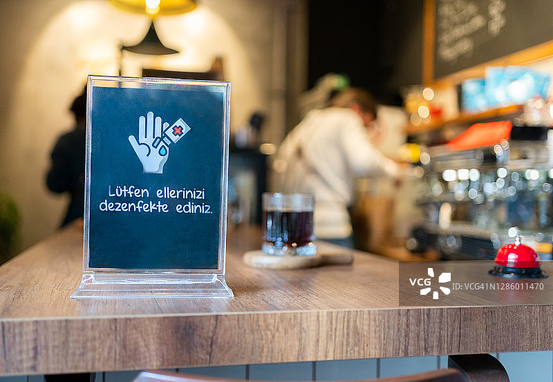 疫情期间现代咖啡馆木质柜台上，带免洗洗手液标志的无菌双手特写图片素材