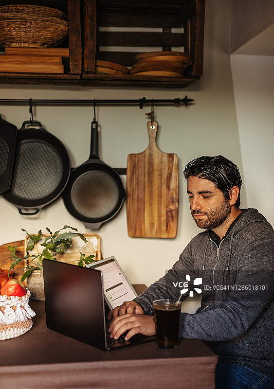 年轻男人在家中厨房用电脑工作图片素材