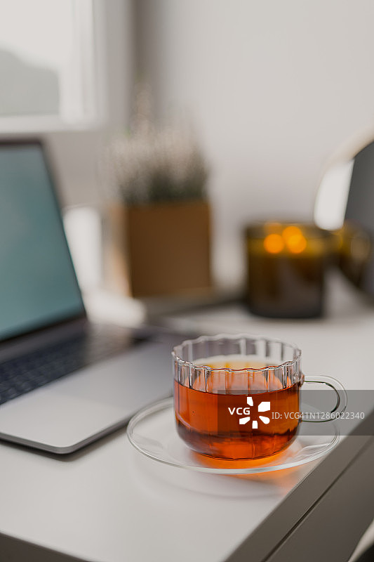 舒适的居家氛围，笔记本电脑旁放着茶杯和蜡烛图片素材