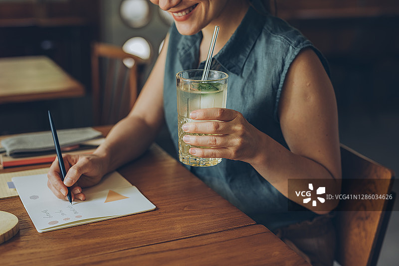 远程办公：自由职业者在咖啡馆喝柠檬水并记录笔记图片素材