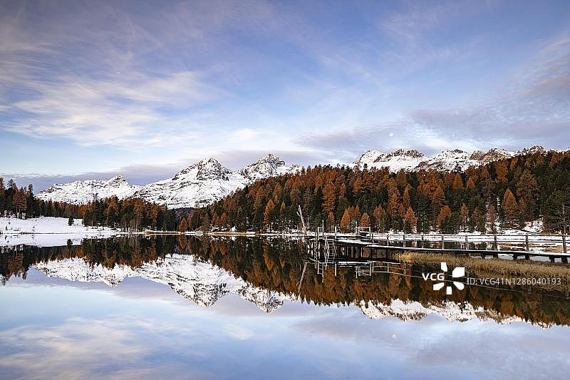 瑞士格里松斯州圣莫里茨的斯塔兹湖中白雪皑皑的山峰和秋天的落叶松倒影图片素材