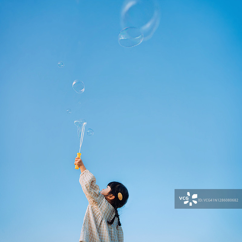 在美丽的蓝天下，于自然公园户外玩肥皂泡泡的可爱亚洲小女孩图片素材