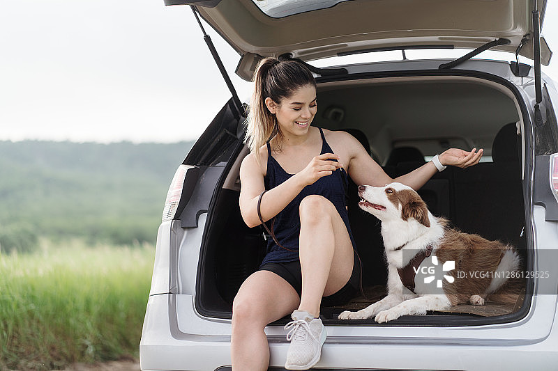 快乐的女人和狗坐在汽车后备箱外图片素材