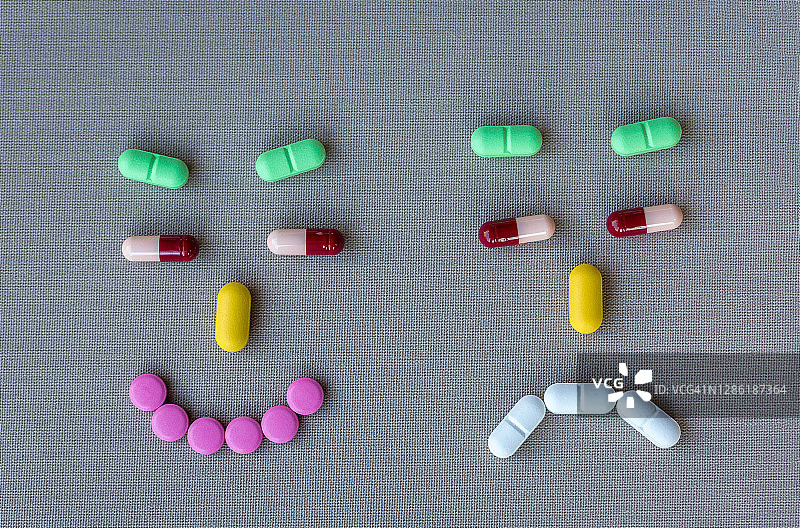 用不同彩色药丸做成的有趣表情，灰色纺织背景上用药丸做成的笑脸和悲伤脸图片素材