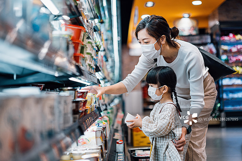 年轻的亚洲母亲和女儿戴口罩在超市购买新鲜有机乳制品图片素材