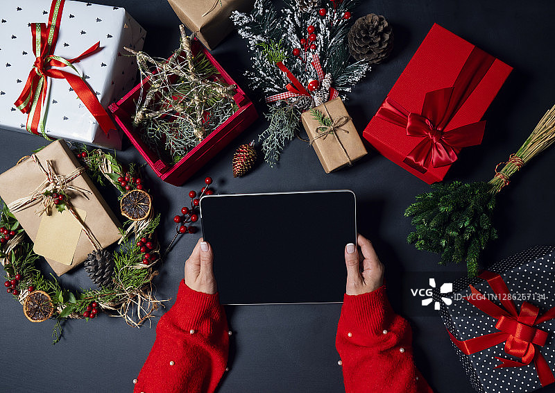在家中手持平板电脑，有圣诞装饰和礼品盒的年轻女子图片素材