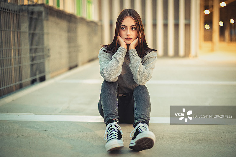 年轻女人独自坐在水泥地上，感到不适图片素材