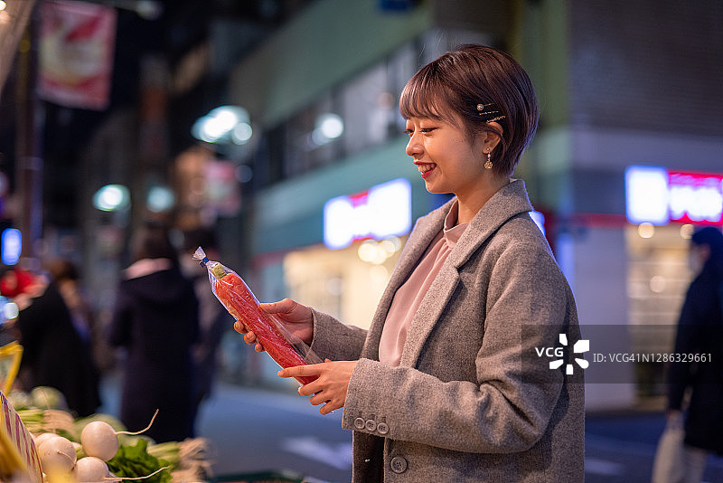 年轻女人夜晚在蔬菜店挑选胡萝卜图片素材