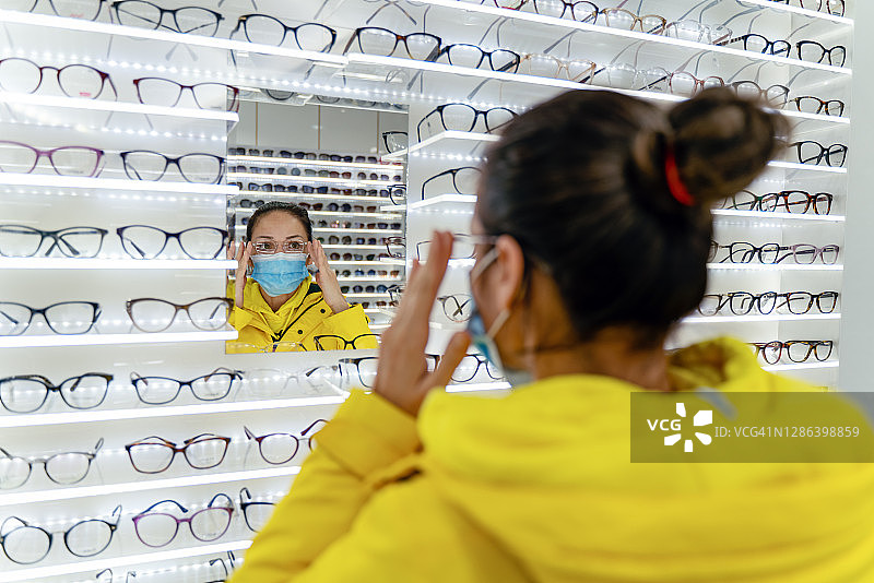 顾客在眼镜店戴着口罩试戴老花镜图片素材