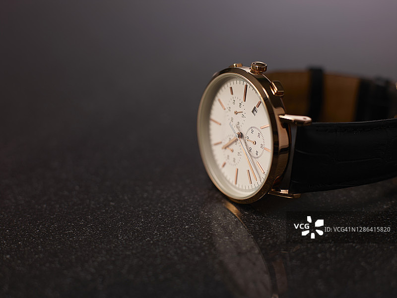深色反光面上棕色皮带金色手表图片素材