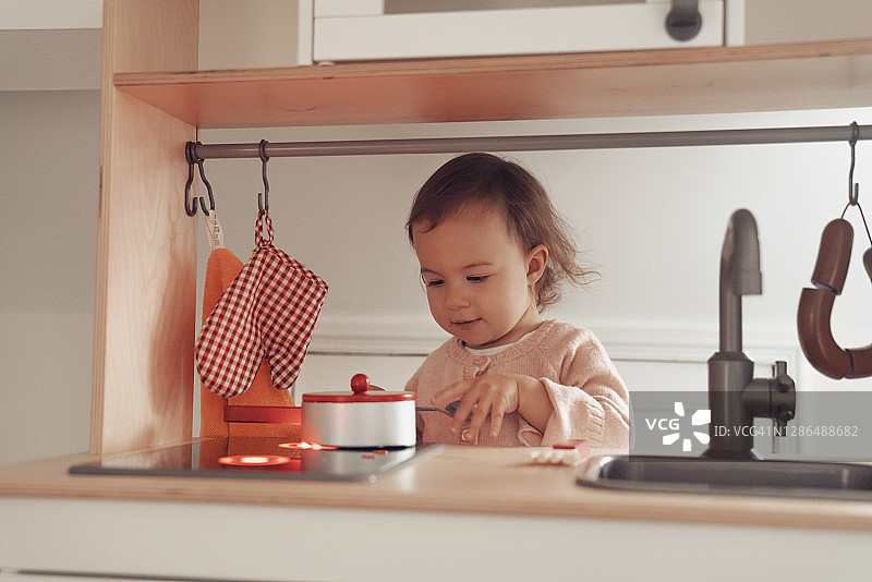 小女孩在家里的玩具厨房做饭图片素材