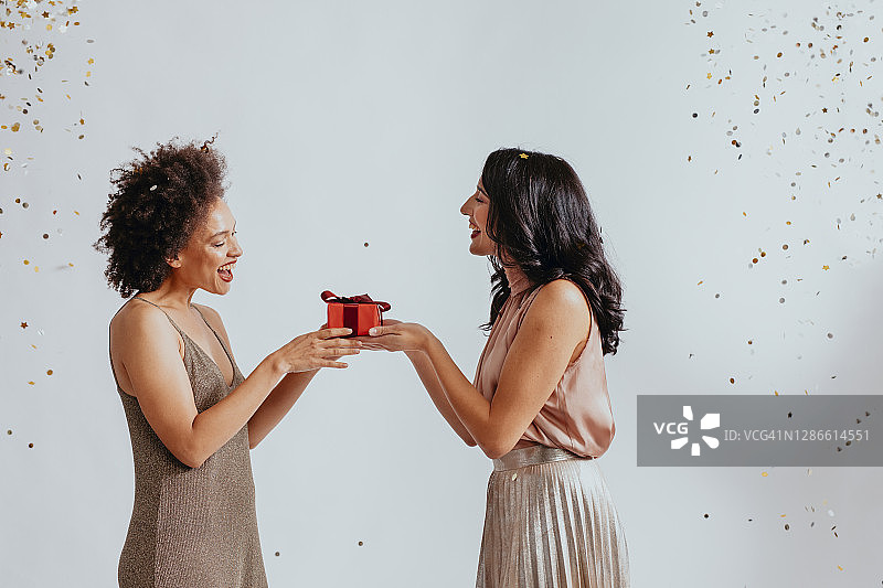 圣诞节：两个年轻女子在派对上交换圣诞礼物图片素材