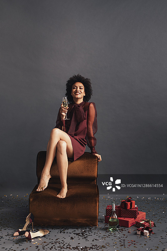 非洲裔美国妇女赤脚坐在地上，手持香槟，周围堆满了圣诞礼物图片素材