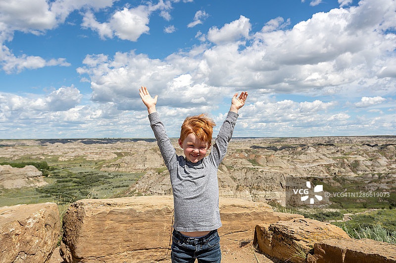 在加拿大艾伯塔省恐龙省立公园荒地中举起双臂的可爱红发男孩图片素材