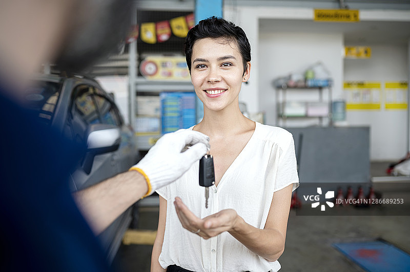 在汽车维修中心的车间里，汽车修理工将车钥匙交给他的女顾客。服务质量，客户满意度图片素材
