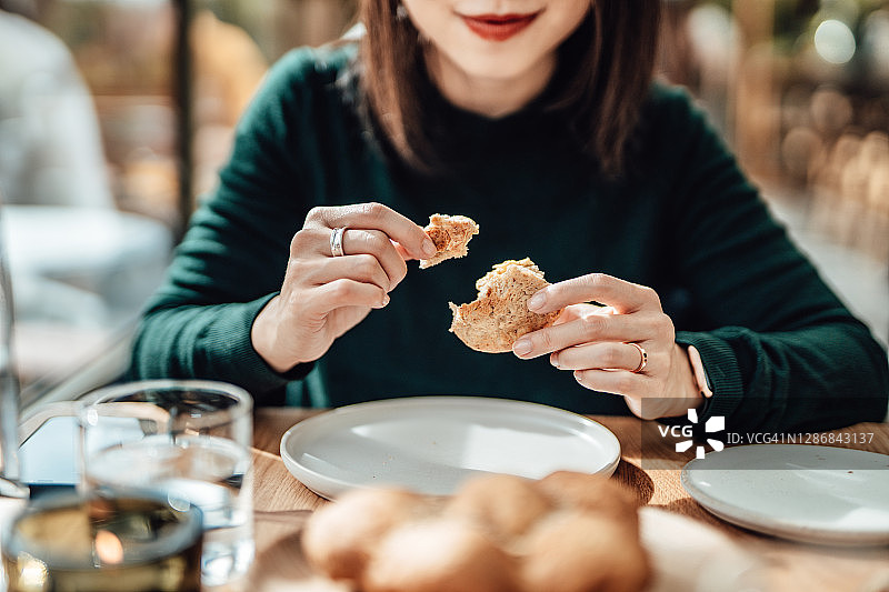 在餐厅吃面包的年轻微笑女子图片素材
