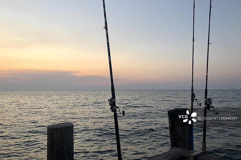 海洋、黄昏天空和日落时分的三根钓鱼竿图片素材