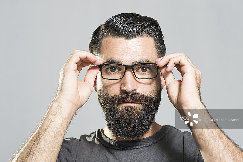 在工作室里对着相机调整眼镜的时髦胡须男人图片素材