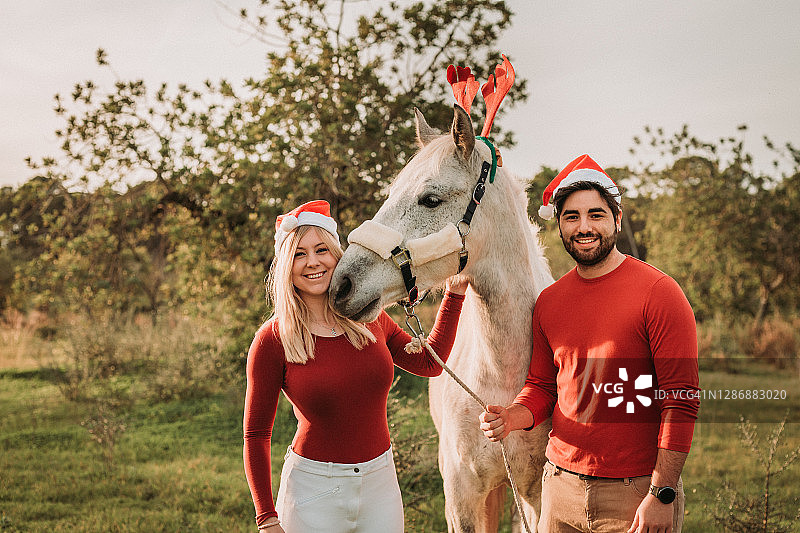 年轻快乐的圣诞情侣与白马在户外图片素材