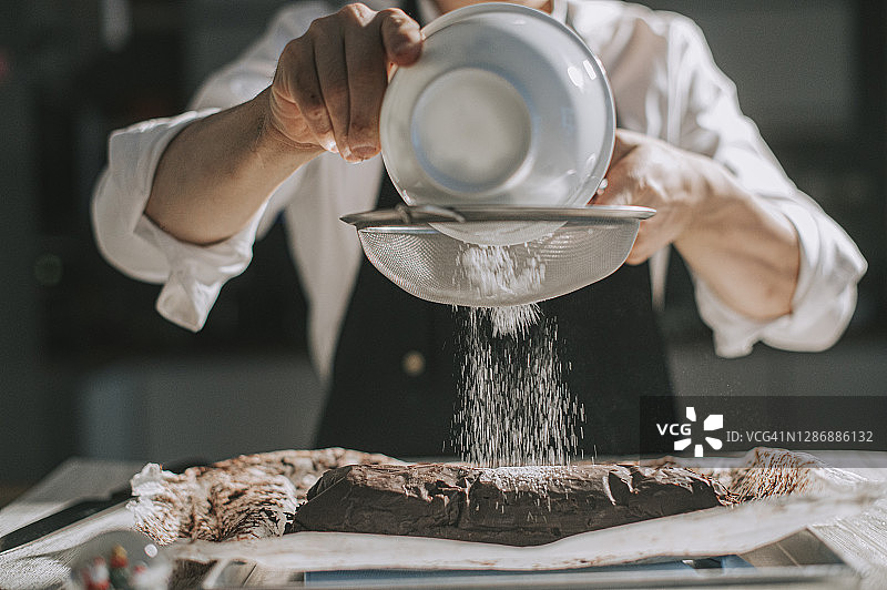 华人甜点师在厨房里为巧克力酥饼撒粉图片素材