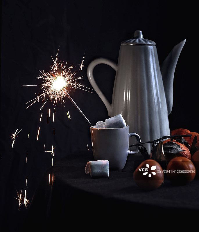 圣诞静物摄影：咖啡壶、棉花糖热饮、橘子和黑色背景上的烟花特写图片素材