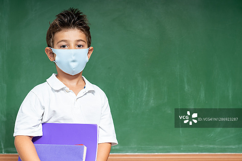 戴防护口罩的小学生站在黑板前的肖像图片素材