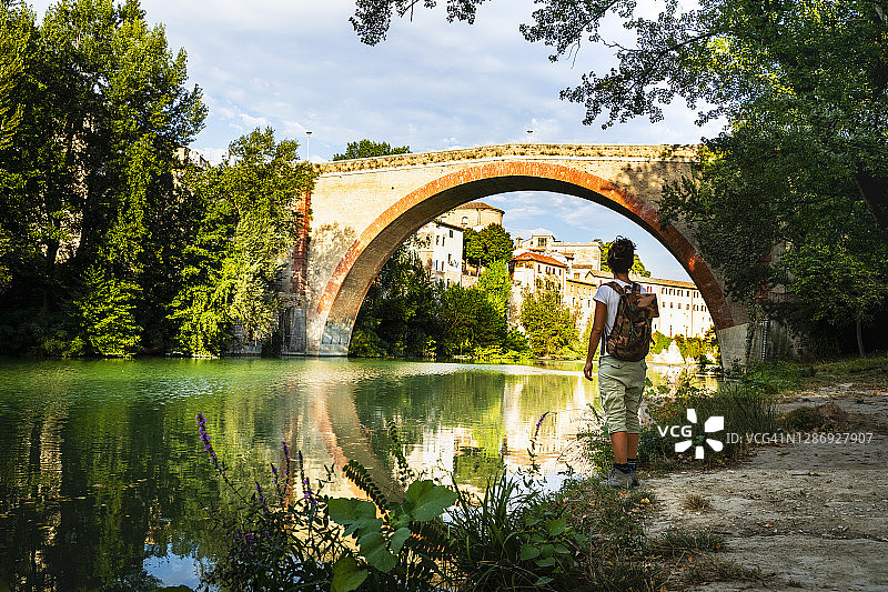 女子站在意大利马尔凯 Fossombrone 的康科迪亚古桥旁图片素材