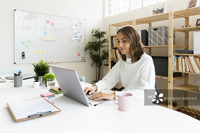 女商人坐在办公室的桌子旁，用笔记本电脑工作图片素材