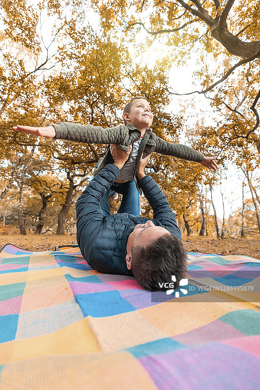 男孩想象和父亲在公园野餐垫上飞翔图片素材