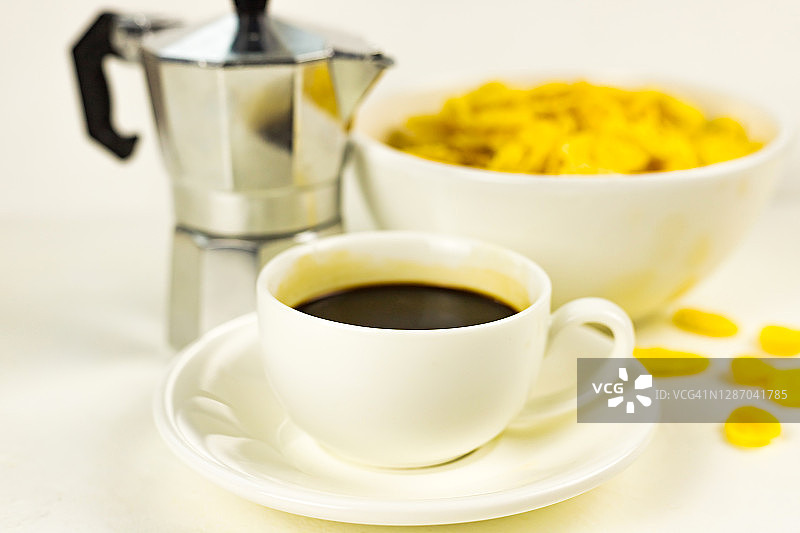 白碗里的玉米片、黑咖啡浓缩咖啡杯、白色背景下的间歇泉咖啡机图片素材