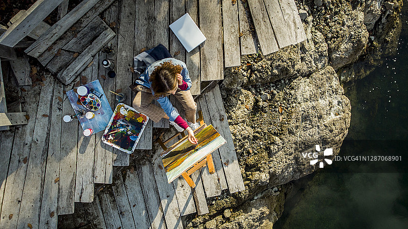 一位年轻艺术家在美丽的湖边大自然中绘画的无人机照片-一位年轻美丽的艺术家受到秋天大自然的启发，创作了她的艺术作品图片素材