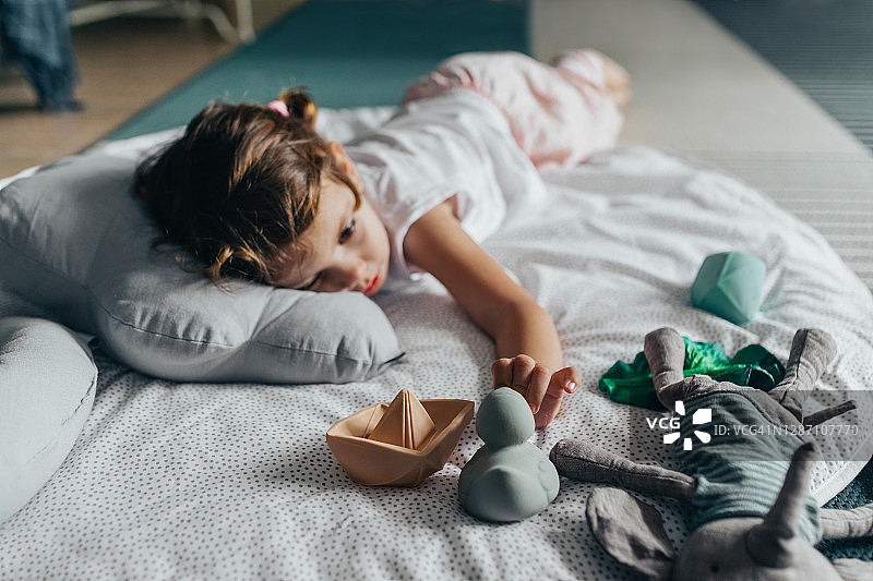 一个可爱的小女孩躺在地板上看着她的玩具图片素材