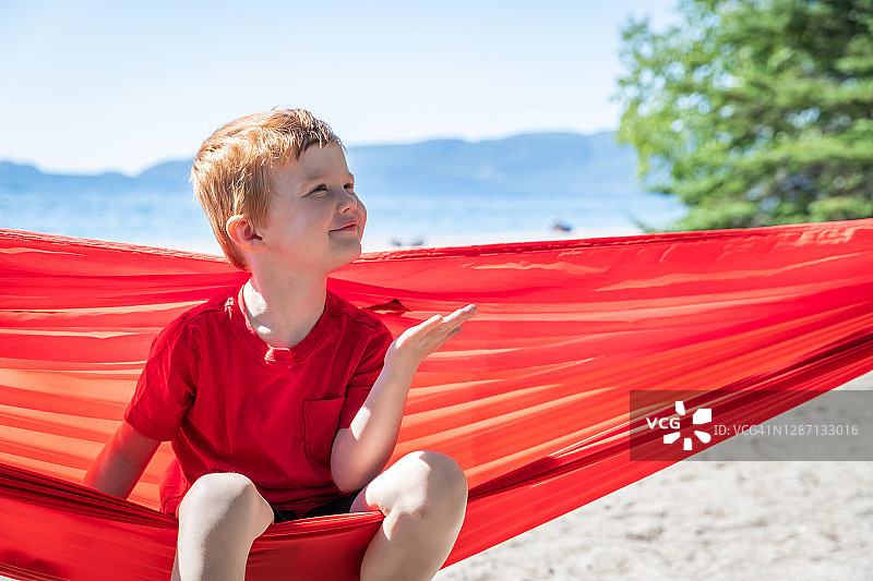可爱的红发儿童在夏季露营地红色吊床上玩耍图片素材