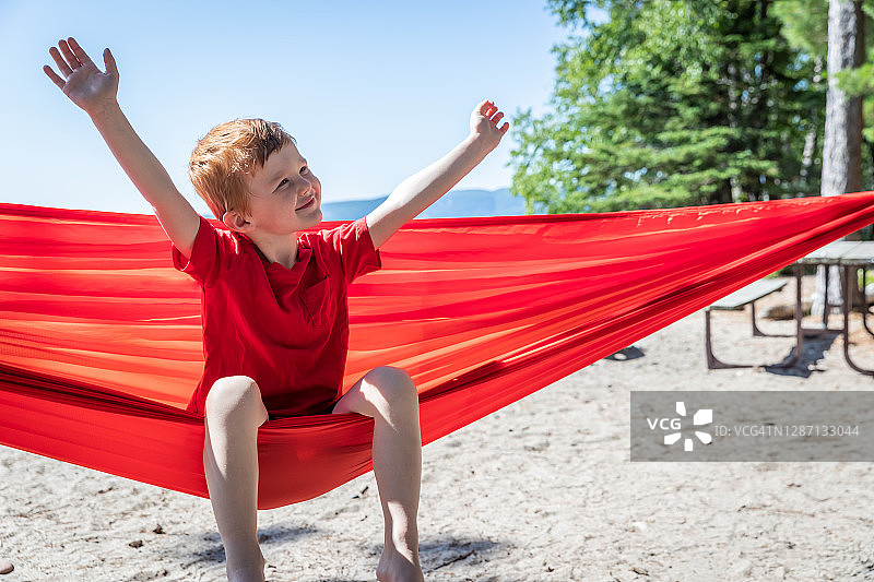 可爱的红发儿童在夏季露营地红色吊床上玩耍图片素材
