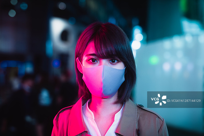 站在夜晚街道霓虹灯下的戴口罩的日本女人图片素材