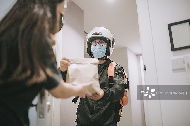 戴头盔和口罩的亚洲华人外卖员按门铃送货图片素材