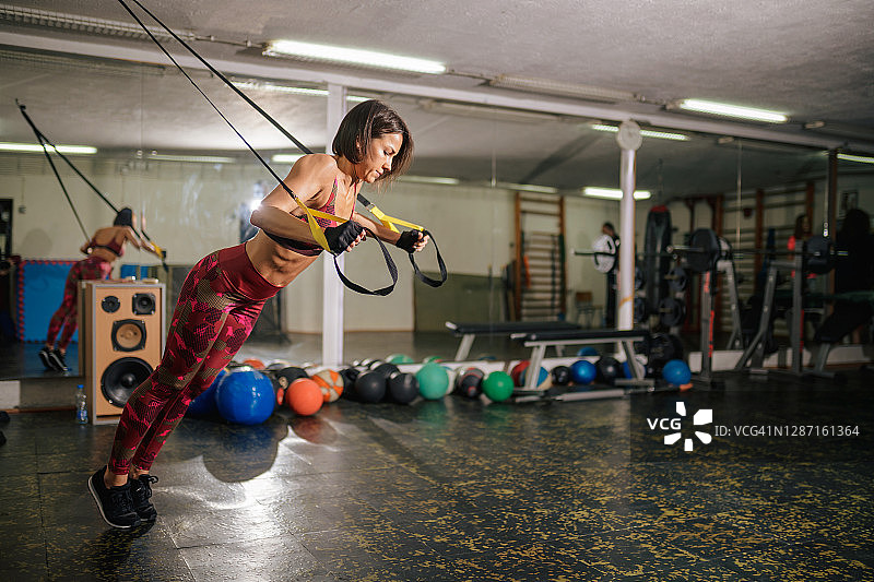 在健身房里手持TRX带并向前倾的女人图片素材