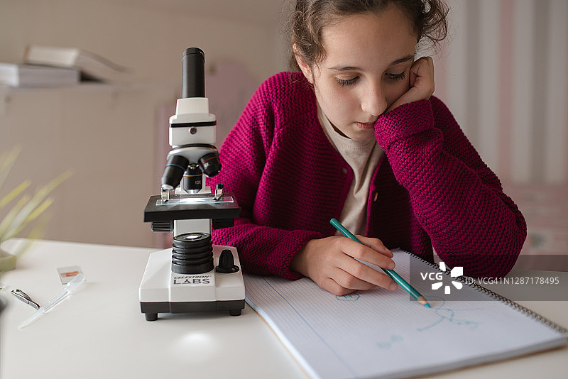 女孩在显微镜下查看后在笔记本上做笔记图片素材