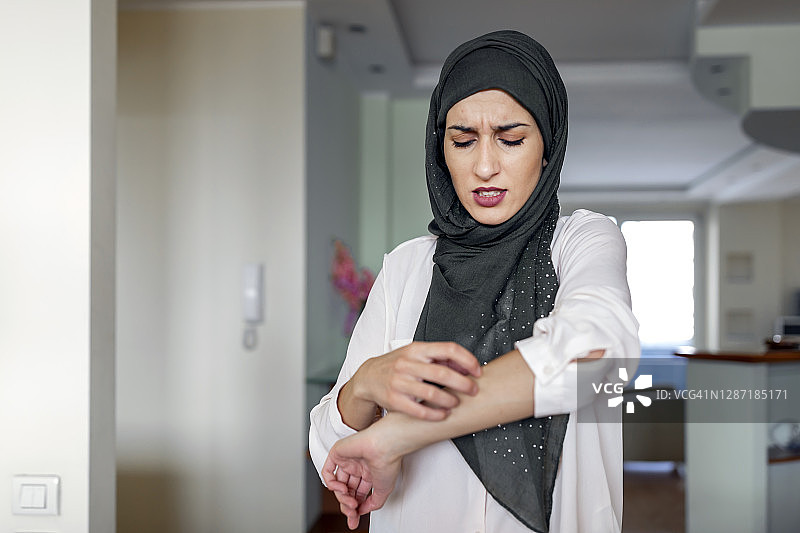 挠手的穆斯林妇女：皮肤干燥，过敏性皮肤炎症，身体护理，真菌感染，皮肤病，湿疹，皮疹，皮肤护理概念；年轻的成年伊斯兰妇女模特图片素材