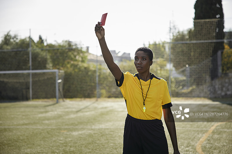 非裔美国人女裁判身穿黄色制服，手持红牌图片素材