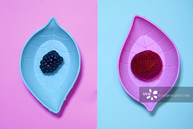 粉色和绿色背景上叶形盘子里的黑莓和草莓特写图片素材