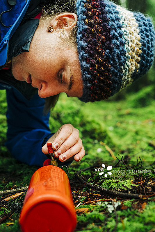 女人在森林里蹲在野营炉燃料瓶和调节器上，调整控制旋钮并点燃炉子特写图片素材