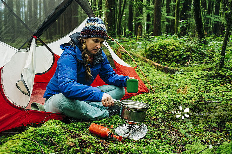 年轻女子在茂密森林的帐篷门口用炉子做饭图片素材